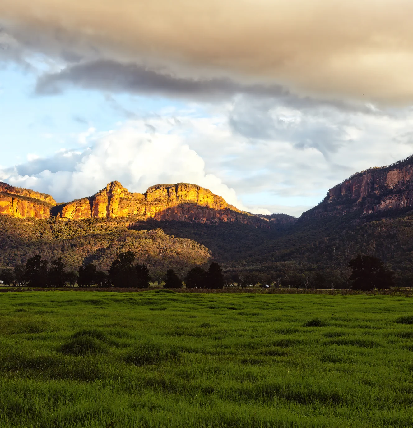 Sunlit sandstone cliff line above a green valley floor